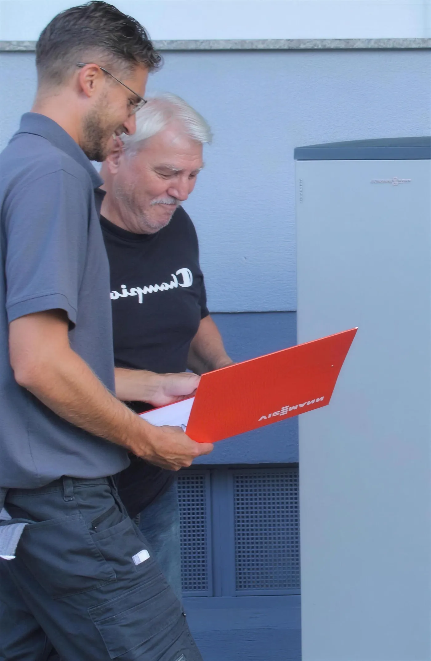 Beratungsgespräch vor einer Viessmann Wärmepumpe, mit Viessmann Unterlagen in der Hand