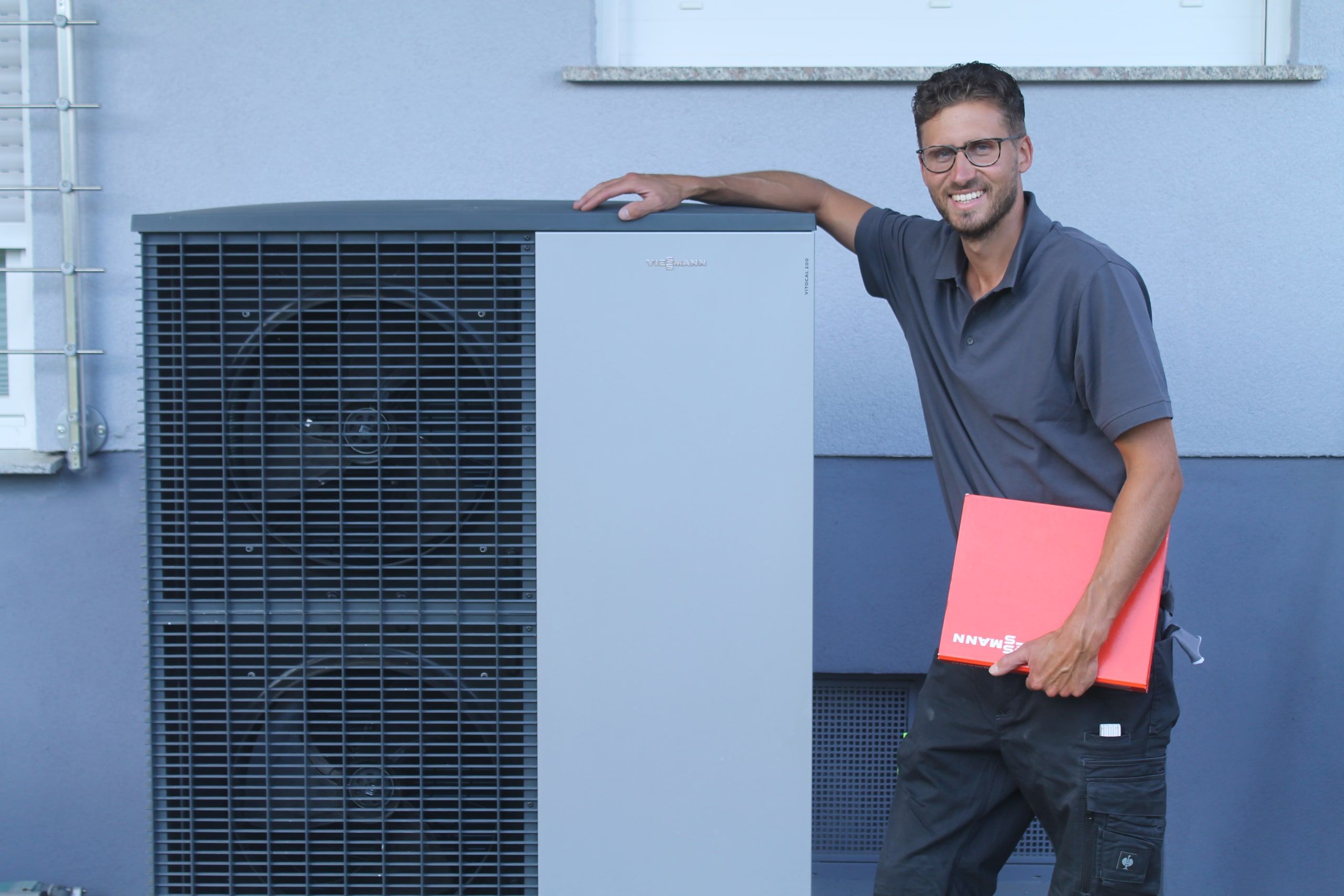 Jan Roth mit Viessmann Mappe neben einer fertig montierten Viessmann Vitocal 200 Wärmepumpe